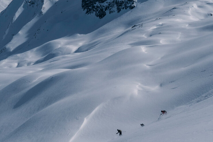 Unberührte Hängen hinab wedeln Skifahrer bei der Abfahrt vom Berg